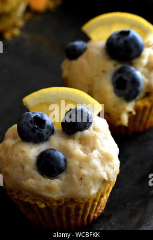 Two homemade keto cupcakes made of almond and walnut flour with lemon and cashew nuts cream decorated with blueberries closeup. Vertical Stock Photo