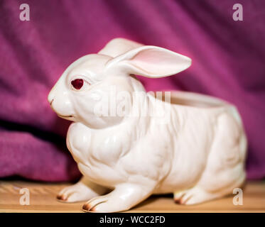 white ceramic bunny with red eyes on pink background and wooden floor Stock Photo