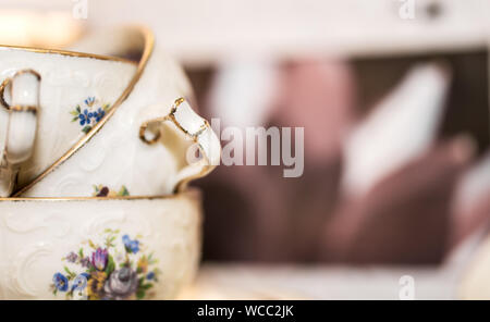 stack of porcelain coffee cups with gold rim and floral design on white pink background. Vintage Stock Photo