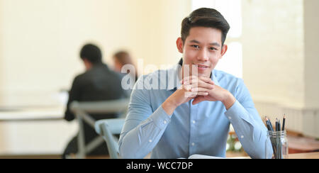 Young businessman smiling confidently at the camera while sitting in modern office room Stock Photo