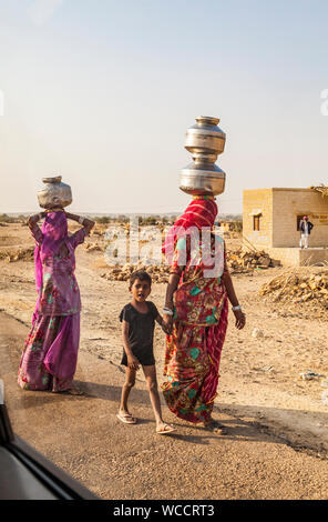Looking through a car window two women and a child walk carrying water jugs balanced on their heads, Thar desert, outside Jaisalmer, Rajasthan, India. Stock Photo