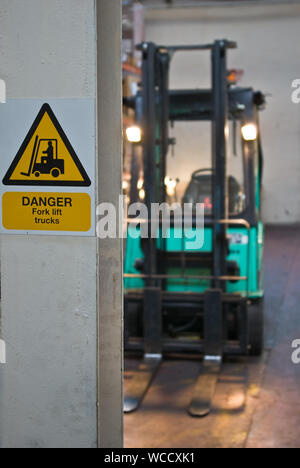 'Danger fork-lift truck' sign on a stanchion with a fork-lift truck in the distance Stock Photo