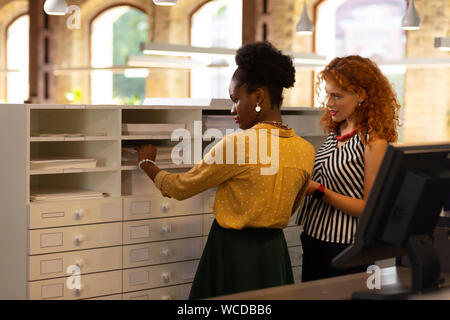 Two workers standing near drawer and looking for folder Stock Photo