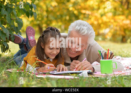 Grandfather and his granddaughter drawing while lying on green grass outdoors Stock Photo