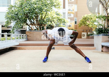 Athletic African American man in blue sneakers doing stretching exercise while training in park on sunny day Stock Photo