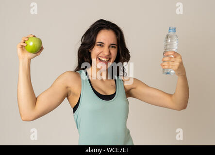 Happy fitness woman smiling holding an apple and water bottle feeling strong and healthy. In Healthy lifestyle, workout and nutrition concept. Portrai Stock Photo