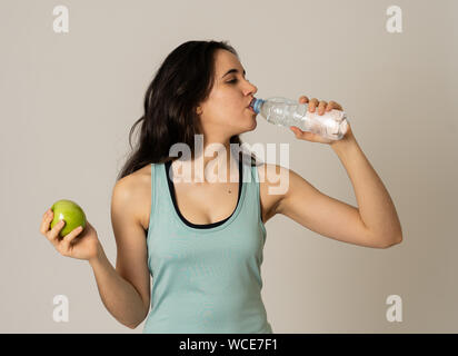 Happy fitness woman smiling holding an apple and water bottle feeling strong and healthy. In Healthy lifestyle, workout and nutrition concept. Portrai Stock Photo