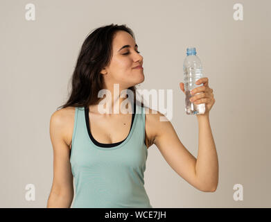 Portrait of beautiful fitness athlete Young latin Woman holding water bottle after work out exercising isolated on grey background in drinking water b Stock Photo