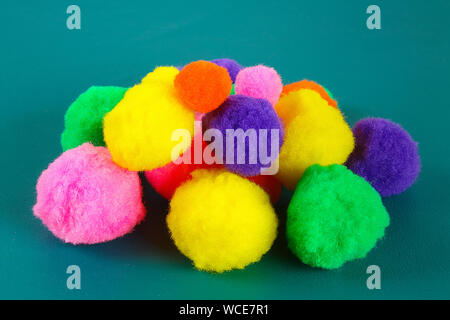 Colored beautiful pompons on a teal background. Assortment of pompons. DIY craft. Stock Photo