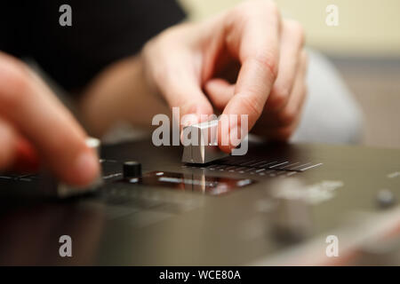 Hip hop dj girl mixes musical tracks with professional sound mixer panel in sound recording studio.Female disc jockey hands on controller device adjus Stock Photo