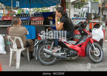 SAMUT PRAKAN, THAILAND, JUN 03 2019, A policeman sits at market and talking to a woman sitting on a motorcycle. Stock Photo