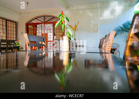 LAHAD DATU BORNEO - MAY 19 2019; Stylish tropical interior home design shady patio dining setting with single red ginger plant flower in bamboo vase r Stock Photo