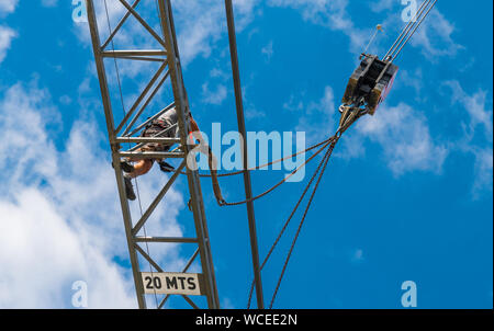 Tower crane installation. Hoist device detail. Work at heights. Working man on steel boom of lifting machine. Blue sky background. Occupational safety. Stock Photo