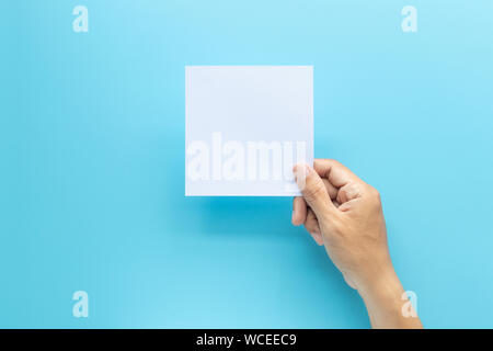 man hand holding blank card paper sheet isolated on blue background with copy space. Stock Photo