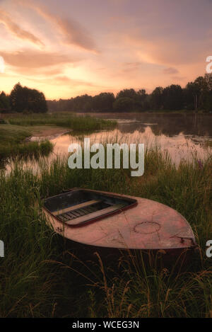 Boat in the grass by the river. Dawn over the river, image in the orange toning. Stock Photo