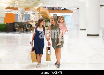 Mother and daughters walking with shopping bags on storefronts background Stock Photo