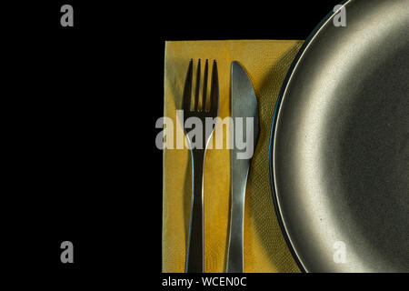 metal fork, knife on yellow napkin and plate on a black background. top view on stainless knife and fork with copy space. Stock Photo