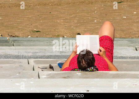 Woman reading a book on the steps on Margate beach, England, Kent. Stock Photo