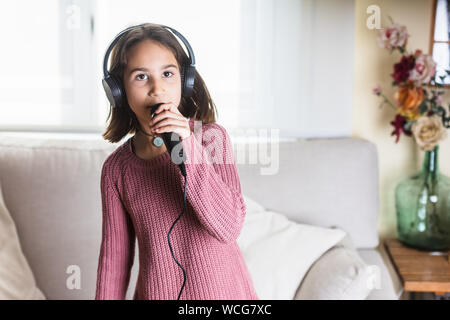Niña cantando feliz con auriculares y micrófono en interior de casa Stock Photo