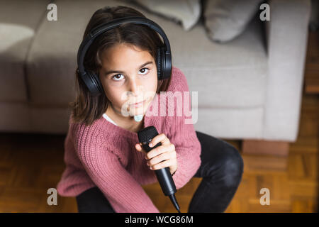 Niña cantando feliz con auriculares y micrófono en interior de casa Stock Photo