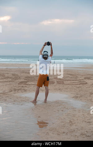 Male photographer taking a photo of the sunset over the ocean at sunset on the beach at Fistral Newquay, in Cornwall, United Kingdom. Stock Photo