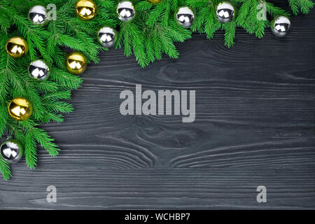 Christmas festive border, New Year decorative frame, shiny gold and silver balls decorations, green fir branches on dark black wooden background Stock Photo