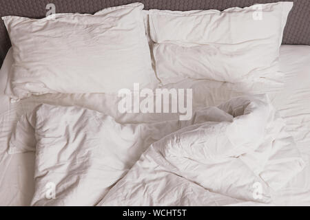 Unmade messy bed with white bedsheet in the morning. Stock Photo