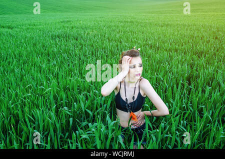 Aggressive make-up girl, battle painting of the face of amazon in a field among green wheat. Feminism, independence, tribe. Stock Photo