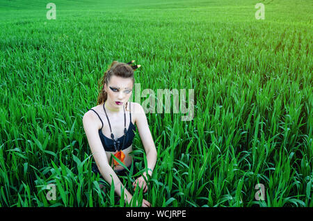 Aggressive make-up girl, battle painting of the face of amazon in a field among green wheat. Feminism, independence, tribe. Stock Photo
