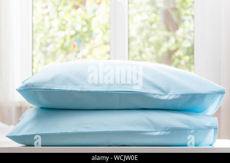 Closeup of two blue pillows lie on a dresser against the background of a blurred window. Stock Photo