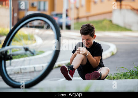 Teenage boy There is a knee injury, as the bike falls while riding. Kid hurt his leg after falling off his bicycle Stock Photo