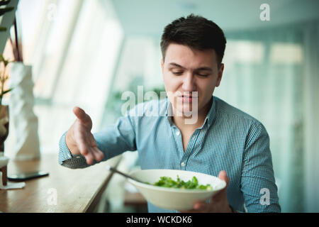 young handsome man is not satisfied with the salad showing it to waiter looking sad . Stock Photo
