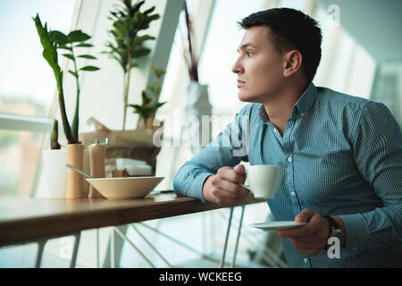 young handsome businessman drinking his hot coffee and eating salad for lunch during break at trendy cafe near office. Stock Photo