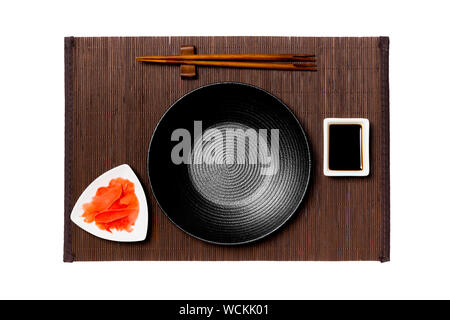Empty round black plate with chopsticks for sushi, ginger and soy sauce on dark bamboo mat background. Top view with copy space for you design. Stock Photo