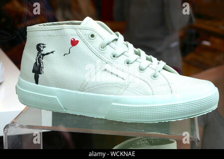 Banksy's most popular work the balloon girl painted on a pair of trainers in a shop widow in Carnaby Street . Stock Photo