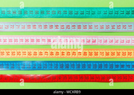 Close up of a group of colorful measure tapes lying in rows as a background. Diet concept on green background. Stock Photo