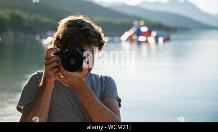Front view of male photographer taking photo with digital camera with calm morning sea in background. Stock Photo