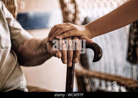 child's hand over old man's hand holding a cane. Stock Photo