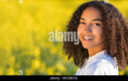 Beautiful mixed race biracial African American girl teenager female young woman smiling and happy in a field of yellow flowers Stock Photo