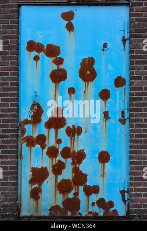 Closed blue neglected rusty door in a stone wall Stock Photo