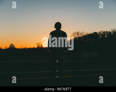 Silhouette Man Standing Amidst Railroad Tracks On Field Against Sky During Sunset