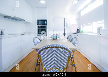 Stylish and brightly lit residential kitchen with dining table. Stock Photo
