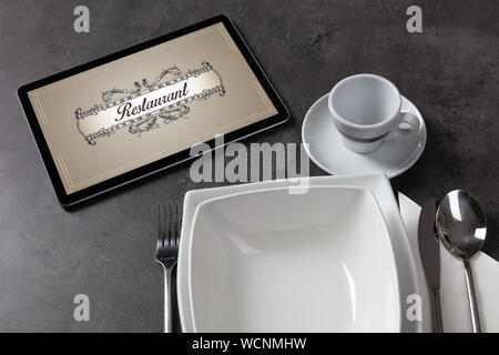 Tablet with stylish restaurant logo and laid table Stock Photo