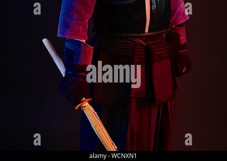 Close up shot, Kendo fighter wearing in an armor, traditional kimono is practicing martial art with shinai bamboo sword, black background. Stock Photo