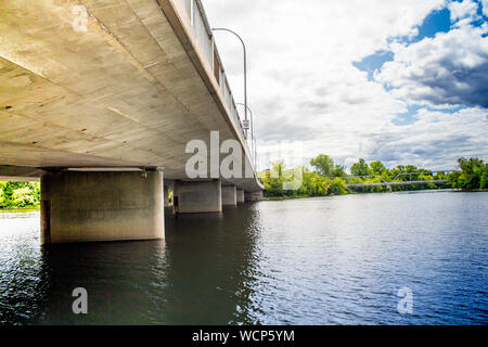 Rippling water of a river flows under a concrete roadway bridge, viewed from below. Stock Photo