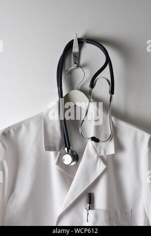 A Doctors White Lab Coat on a  hanger on a Hook with Stethoscope, pen in pocket. Stock Photo