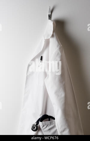 A Doctors White Lab Coat and Hanging on a Hook with Stethoscope in pocket. Stock Photo