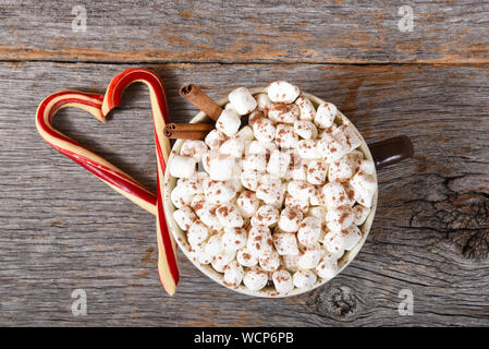 High angle shot of a large mug of hot cocoa with marshmallows and two candy canes forming a heart on a rustic wood table. Stock Photo