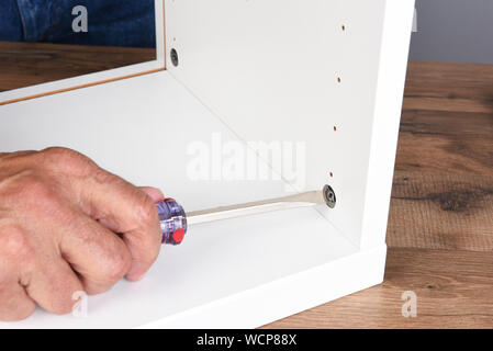 Closeup of a man assembling a DIY piece of furniture. The man is using a screwdriver to tighten a piece of hardware. Stock Photo