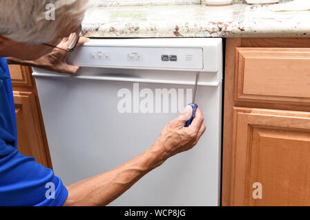 Closeup of a appliance repairman using a screwdriver to remove the control panel on a broken dishwasher. Stock Photo